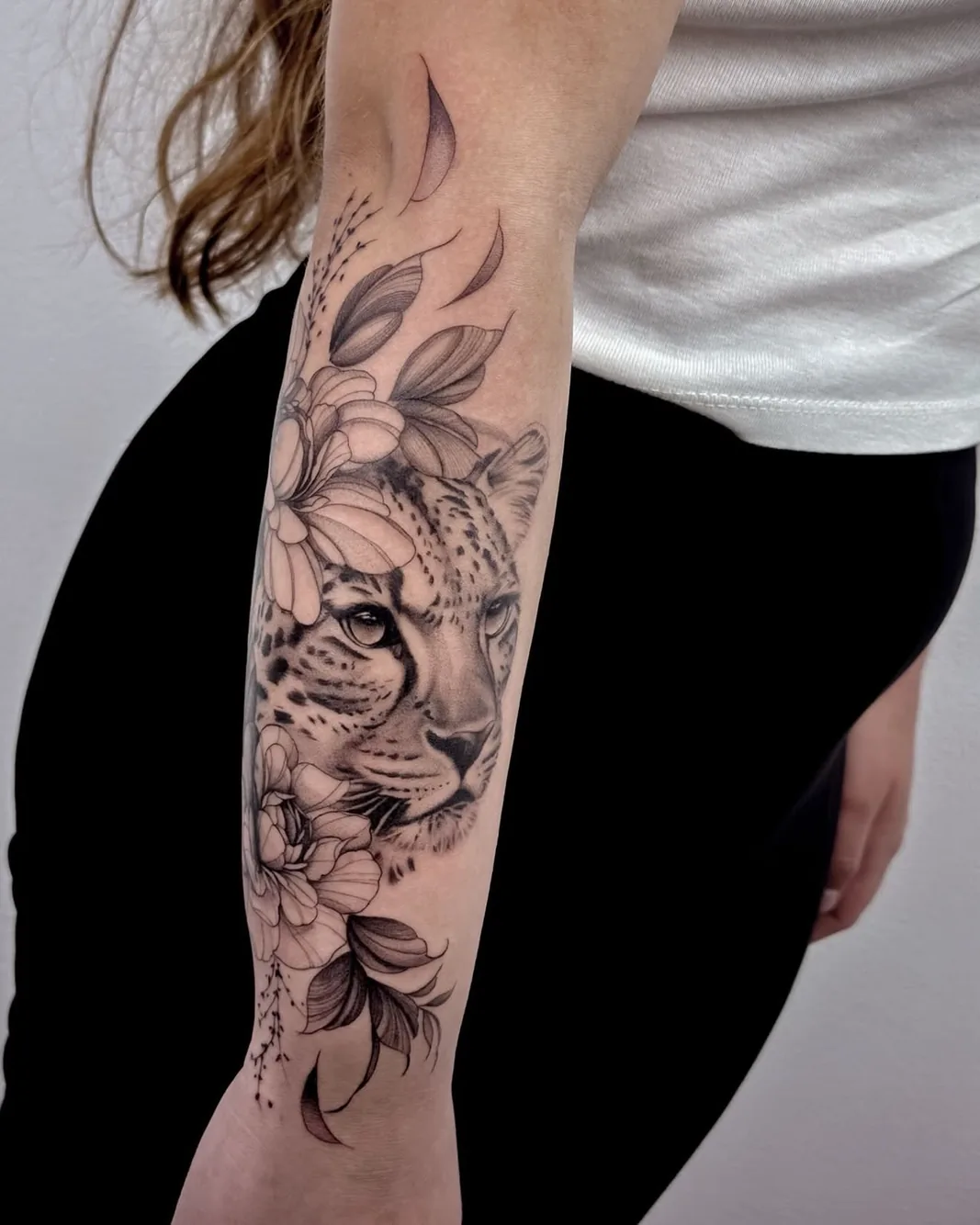 Botanical leopard portrait framed by fine line flowers tattoo on the forearm
