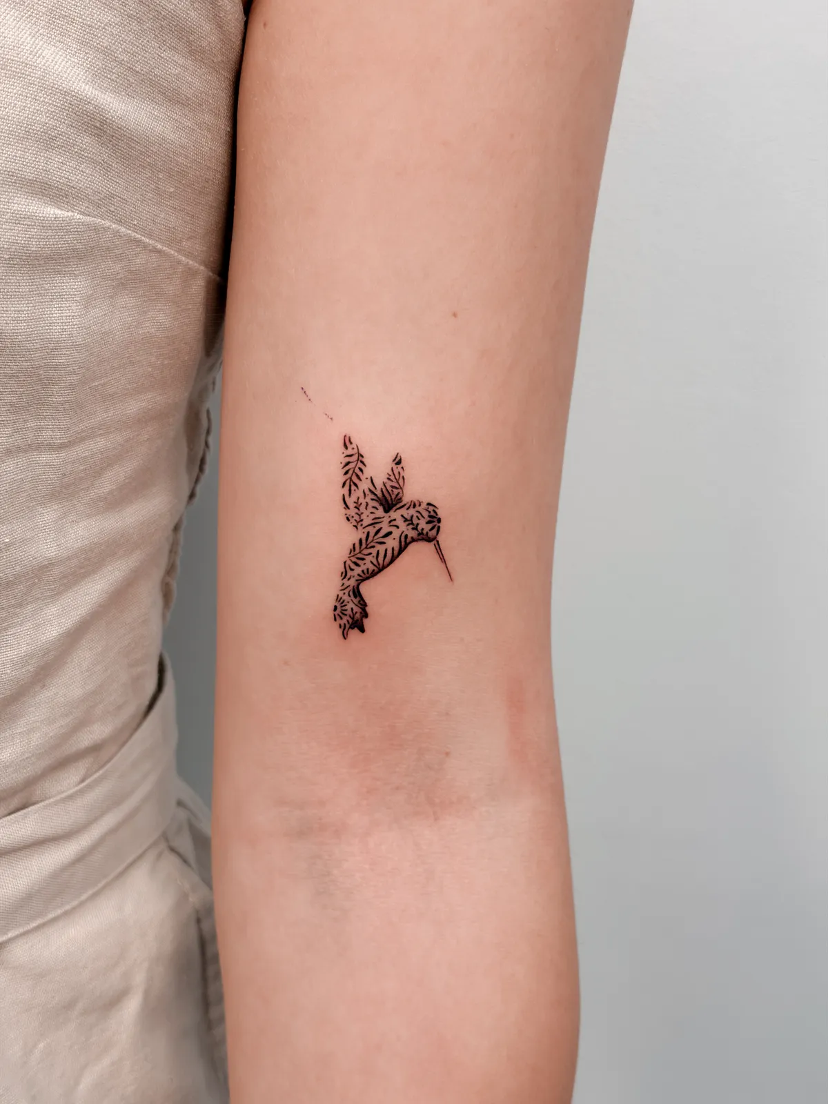 Delicate fine line hummingbird arm tattoo by Hugo Gonzalez